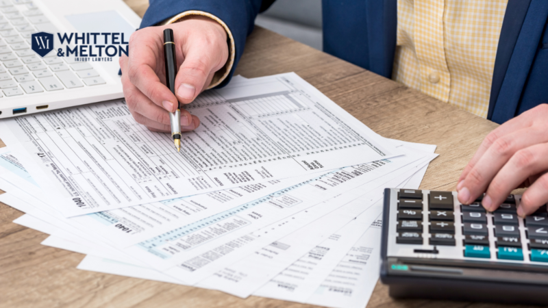 Man filling out tax forms, using a calculator, with the Whittel & Melton Injury Lawyers logo overlaid. Image is used for content about Fort Lauderdale tax evasion and criminal defense attorney Florida.